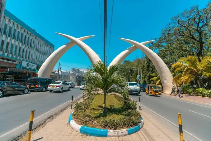The Mombasa Tusks on Moi Avenue, with traffic and a tuk-tuk passing the palms